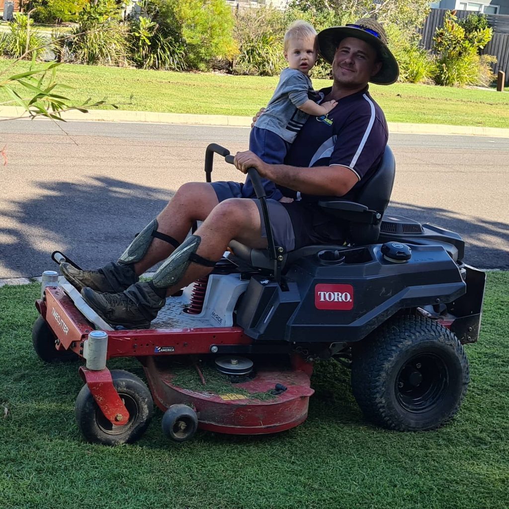 Regular Mowing & Why It's Important - man and child sitting on lawn mower